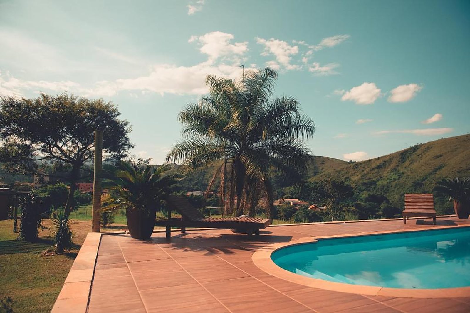 Piscina ao ar livre com palmeira e espreguiçadeira, com a serra ao fundo