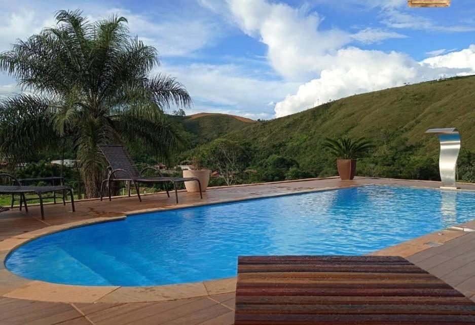 Piscina azul com espreguiçadeiras e cascata de inox, com morros verdes ao fundo
